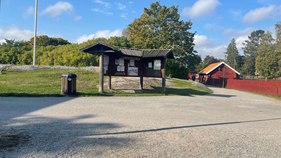 En vägkorsning med grusade vägar. I korsningen står en anslagstavla och ett rött hus skymtar i bakgrunden.