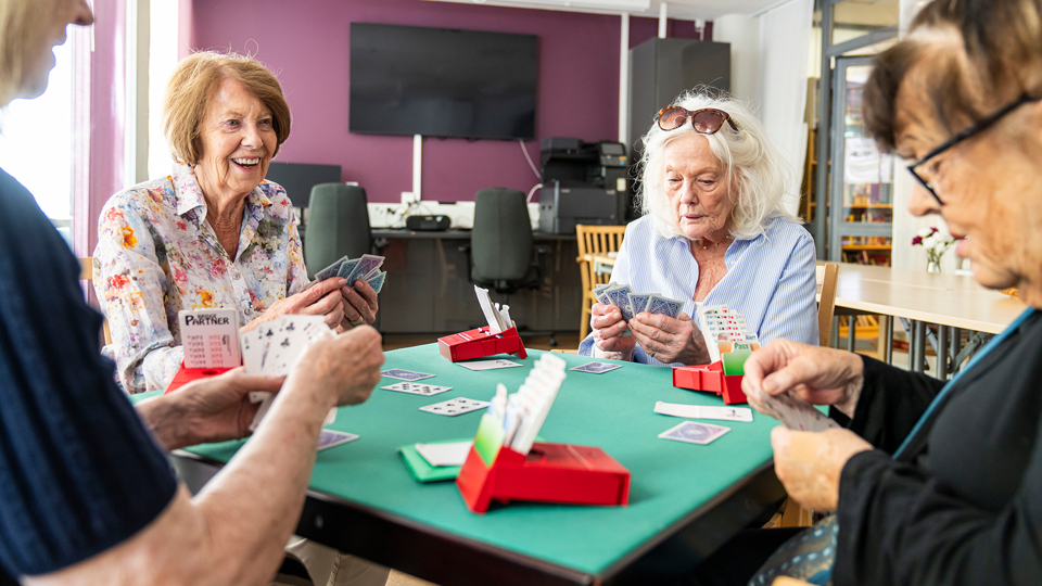 Fyra kvinnor runt ett litet bord spelar kortspelet Bridge
