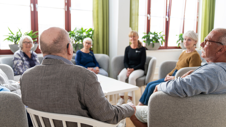 En grupp män och kvinnor sitter i en soffgrupp runt ett bord och samtalar.
