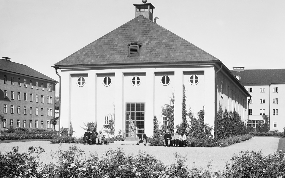 Människor sitter utanför en stor byggnad på en gård.
