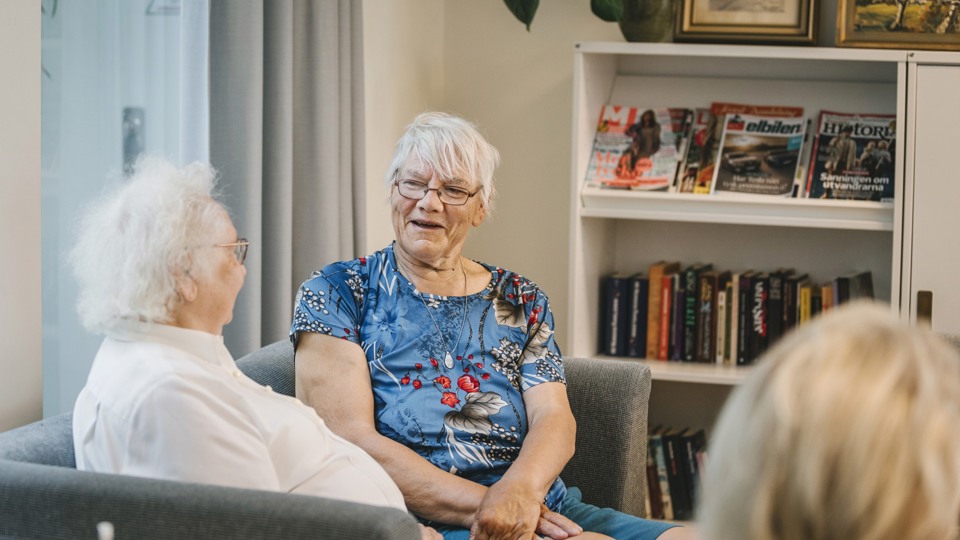 Två kvinnor som sitter i fåtöljer och pratar framför ett bibliotek