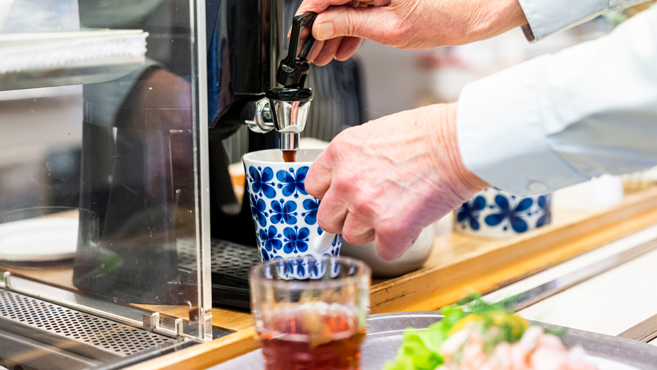 En person målar en blomskiss med gul färg, med penslar och vattenburk på bordet.